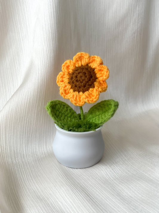 Crocheted sunflower in a small white pot on a light fabric background